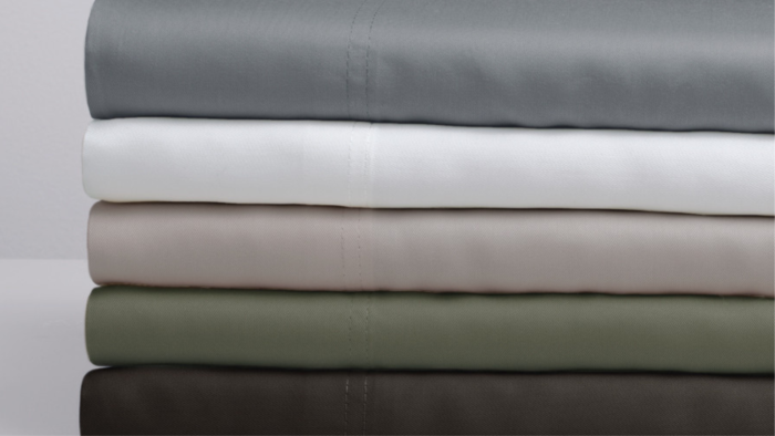 Luxurious gradient bed linens in gray, white, beige, and olive on a minimalist surface.