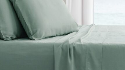 Serene bedroom with muted green linens, plush pillows, and peaceful water view.