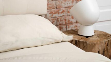 Cozy rustic bedroom with cream bed, brick wall, tree stump nightstand, and modern lamp.