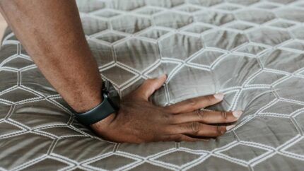 Close-up of textured mattress with hand pressing down, highlighting softness and geometric pattern.
