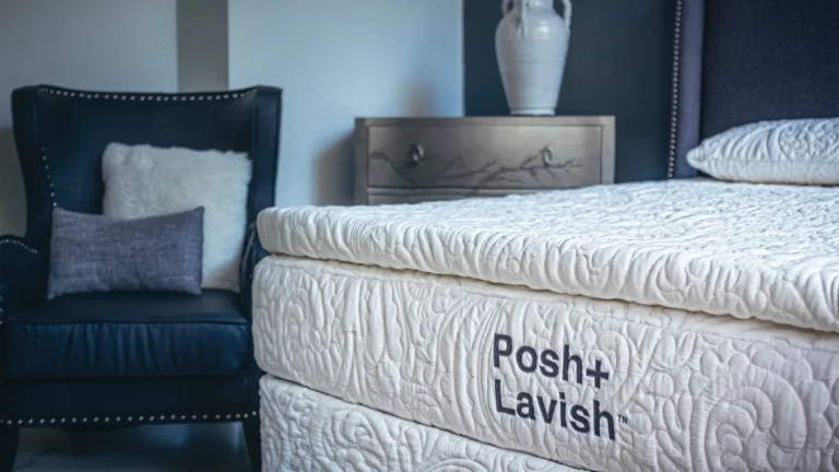 Luxurious bedroom with Posh+Lavish mattress, navy armchair, and elegant metallic nightstand.