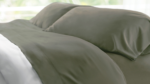 Olive-green satin pillows and white sheet create a serene bedroom retreat.