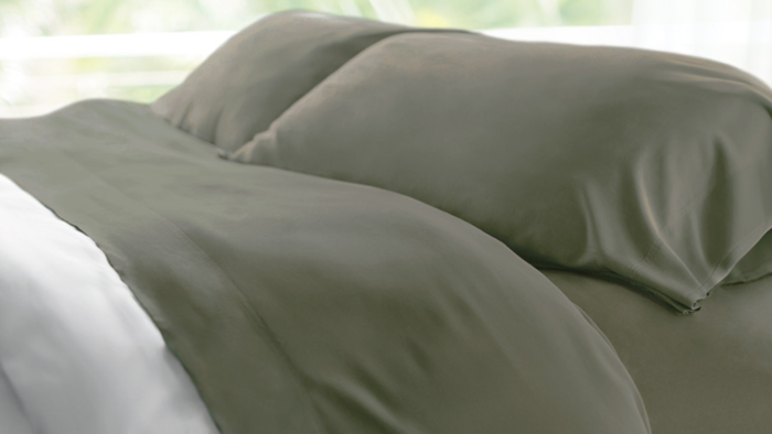 Olive-green satin pillows and white sheet create a serene bedroom retreat.