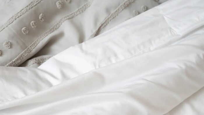 Elegant white comforter with grey textured throw in serene, inviting bedroom setting.