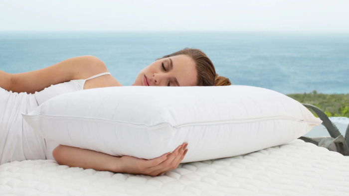 Woman relaxes on balcony bed overlooking tranquil ocean, basking in gentle daylight.
