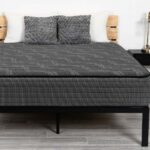 Modern bedroom with gray mattress, black metal frame, wooden nightstands, and decorative elements.