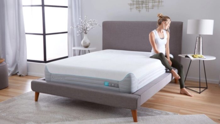 Young woman reading in a serene, modern bedroom with gray upholstered bed.