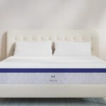 Stylish cream-upholstered bed with tufted headboard, light wood nightstands, and blue-accented mattress.