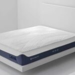 Modern ergonomic mattress on minimalist wooden frame against white wall for serene bedroom.