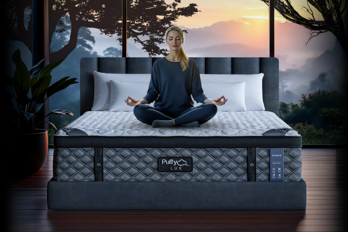 Woman meditating on Puffy Lux mattress with forest sunrise view in serene bedroom.