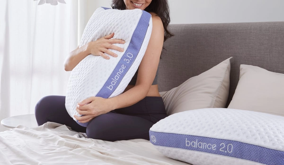 Woman joyfully hugging Balance 2.0 pillow in serene, sunlit bedroom for restful living.