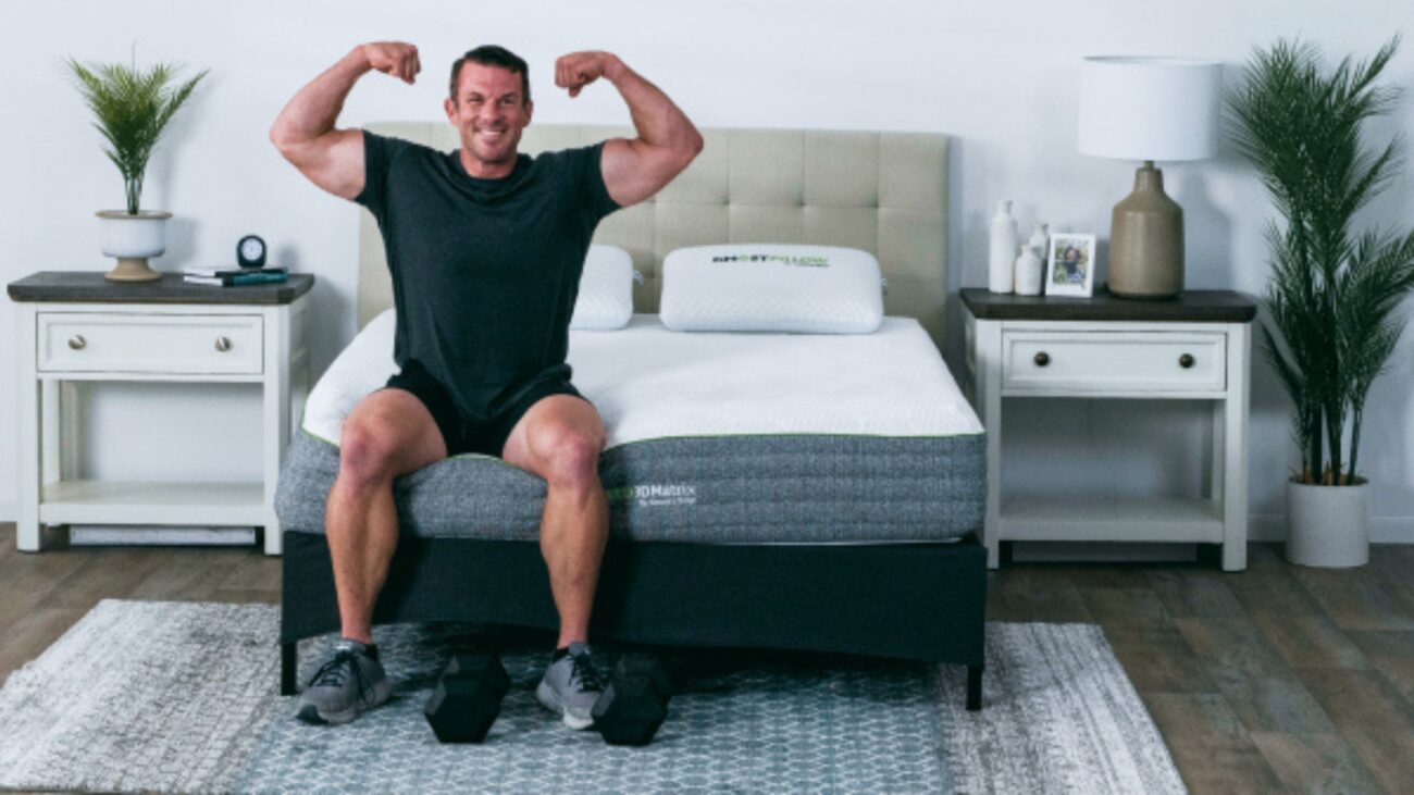 Athletic man on designer bed in cozy, plant-filled bedroom promoting fitness and relaxation.