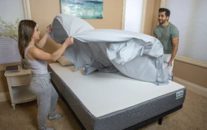 Couple making a bed together in a sunlit, cozy bedroom atmosphere.