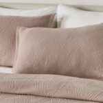 Cozy bed with taupe geometric coverlet, matching pillows, white sheets, and minimal headboard.
