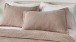 Cozy bed with taupe geometric coverlet, matching pillows, white sheets, and minimal headboard.