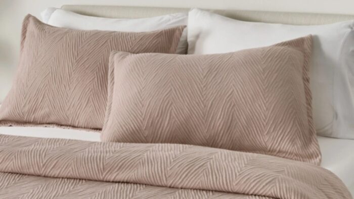 Cozy bed with taupe geometric coverlet, matching pillows, white sheets, and minimal headboard.