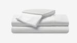 Luxurious white cotton bedding, textured edges, stacked pillowcases; cozy, serene sleep setting.
