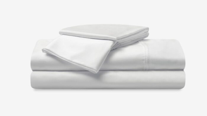 Luxurious white cotton bedding, textured edges, stacked pillowcases; cozy, serene sleep setting.