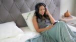 Woman on bed enjoys music with headphones in serene, cozy bedroom setting.
