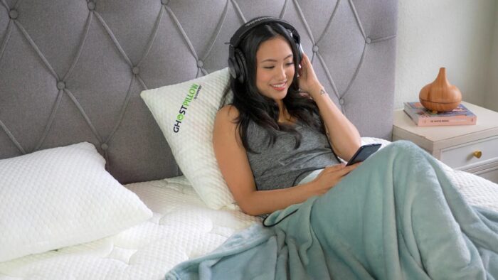 Woman on bed enjoys music with headphones in serene, cozy bedroom setting.