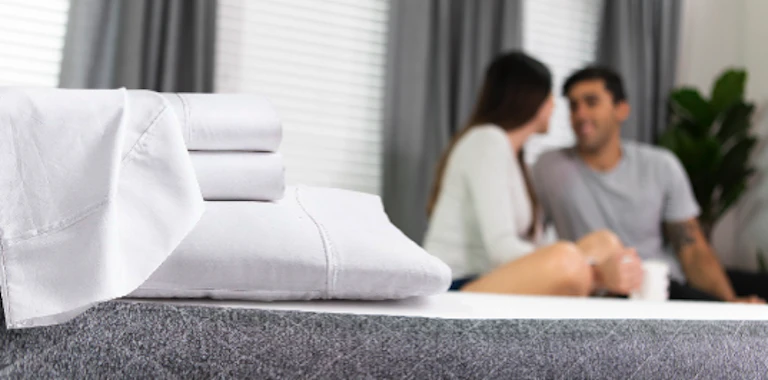 Cozy bedroom with crisp linens, intimate couple, soft lighting, and a tranquil plant.