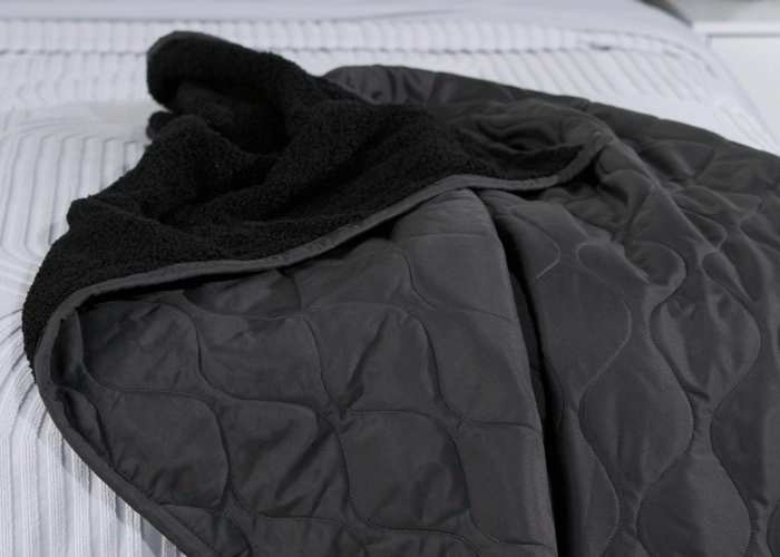 Black quilted blanket with plush lining on tidy striped bed for cozy ambiance.