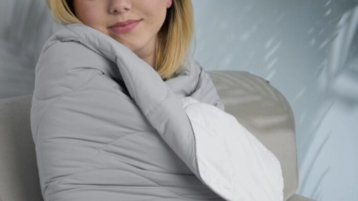 Young woman relaxing on a couch with a warm gray and white blanket.