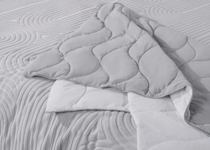 Cozy gray quilt on bed with soothing wavy patterns for relaxation and aesthetic appeal.