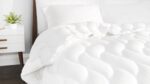 Cozy bed with luxurious white comforter, wooden headboard, and minimalist decor for serene ambiance.