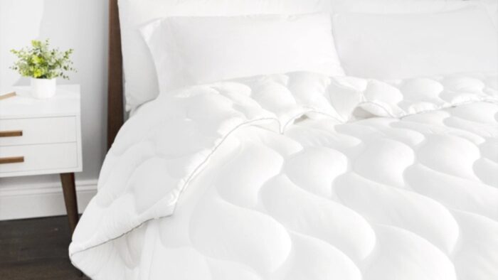 Cozy bed with luxurious white comforter, wooden headboard, and minimalist decor for serene ambiance.