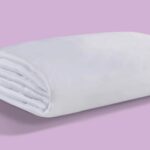Plush white blanket on pastel purple background; cozy, serene, and inviting.