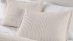 Elegant cream swirl pillows on a white bed for a serene, stylish bedroom setting.