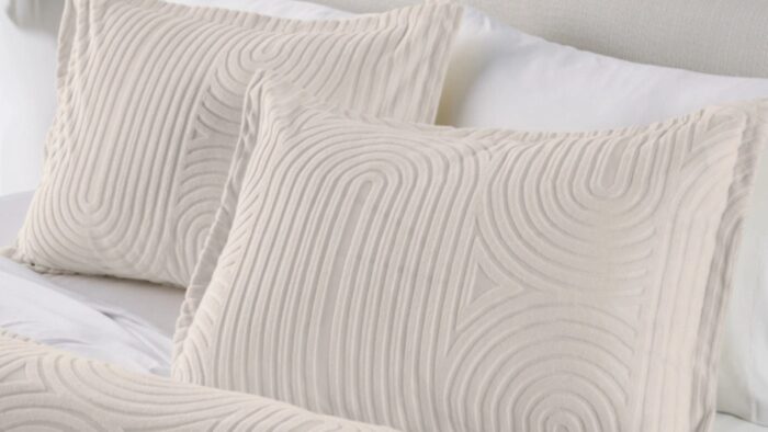 Elegant cream swirl pillows on a white bed for a serene, stylish bedroom setting.