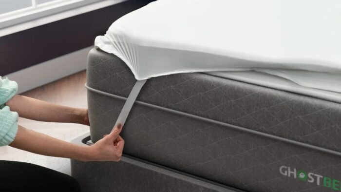 Person securing a smooth fitted sheet on a modern mattress under natural sunlight.