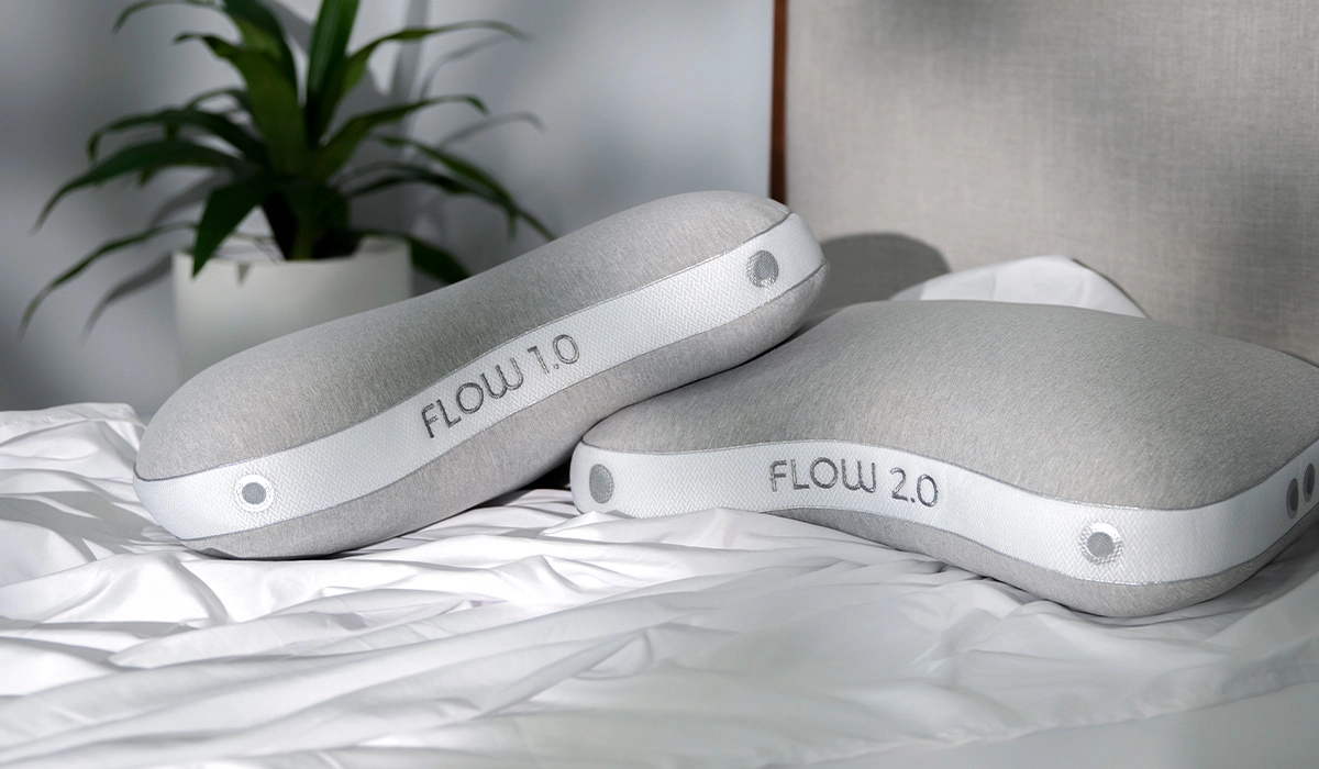 Modern ergonomic pillows on white bedding with plant accent in serene bedroom.