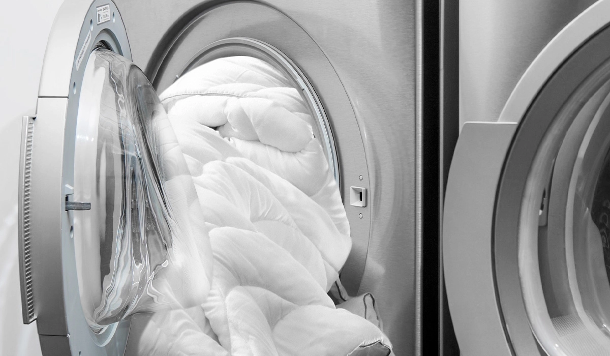 Quilted white comforter in sleek metallic washing machine with open door.