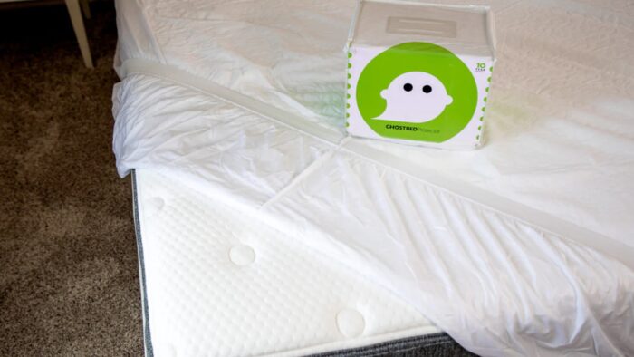Modern bed with memory foam protector and whimsical ghost-themed box on cozy beige carpet.