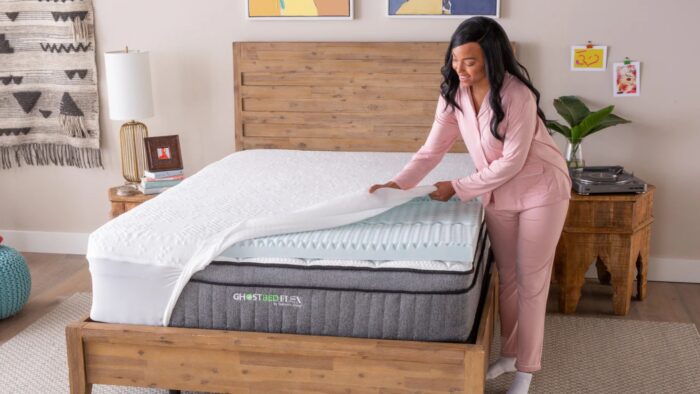 Woman in pink pajamas adjusts hybrid mattress in a stylish bedroom with serene ambiance.