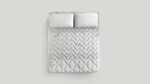 Queen-size bed with gray chevron quilt and plush white pillows for modern comfort.
