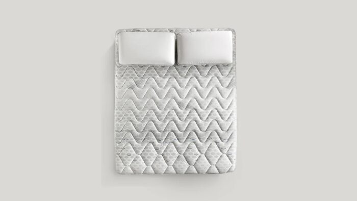 Queen-size bed with gray chevron quilt and plush white pillows for modern comfort.