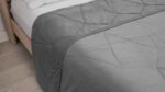 Gray quilt with diamond pattern on wooden bed frame in serene bedroom.