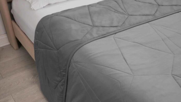 Gray quilt with diamond pattern on wooden bed frame in serene bedroom.