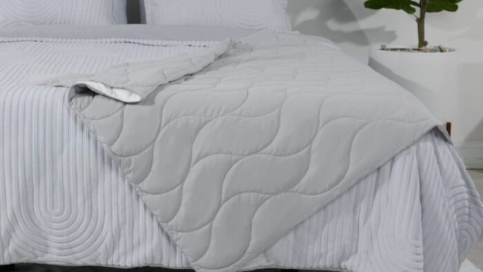 Minimalist bed with gray quilt, striped sheets, pillows, and greenery for a tranquil atmosphere.