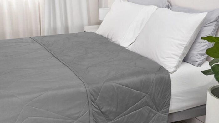 Neatly made bed with gray quilted blanket and white pillows in serene bedroom setting.