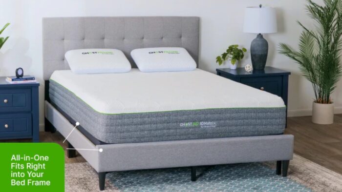 Modern bedroom with gray upholstered bed, blue nightstand, plants, and branded pillows.