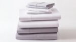 Luxurious gray and white bed linens, neatly stacked, showcasing quality and sophisticated simplicity.