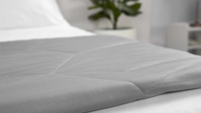 Modern gray quilted blanket on bed with white sheets and green plant nearby.