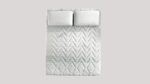 Modern mattress with wavy texture and plush pillows set against a gray backdrop.