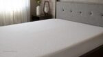 Elegant gray bed frame with white mattress in serene, sunlit bedroom.