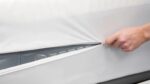 Unzipping white cover reveals protective mesh, suggesting appliance or machinery beneath.